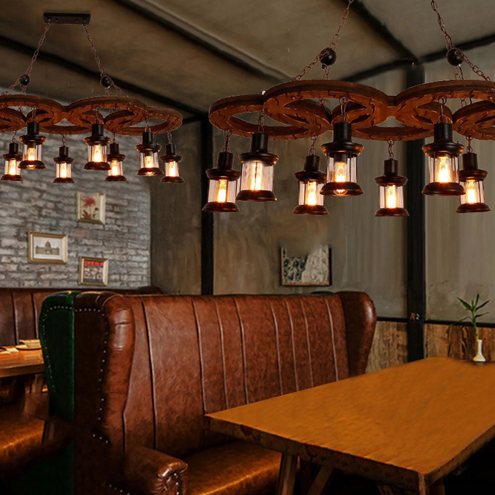 Vintage industrial wood and metal chandelier hanging from the ceiling in a rustic farmhouse interior setting. The room features wooden furniture including a table and chairs, with elements of interior design visible.