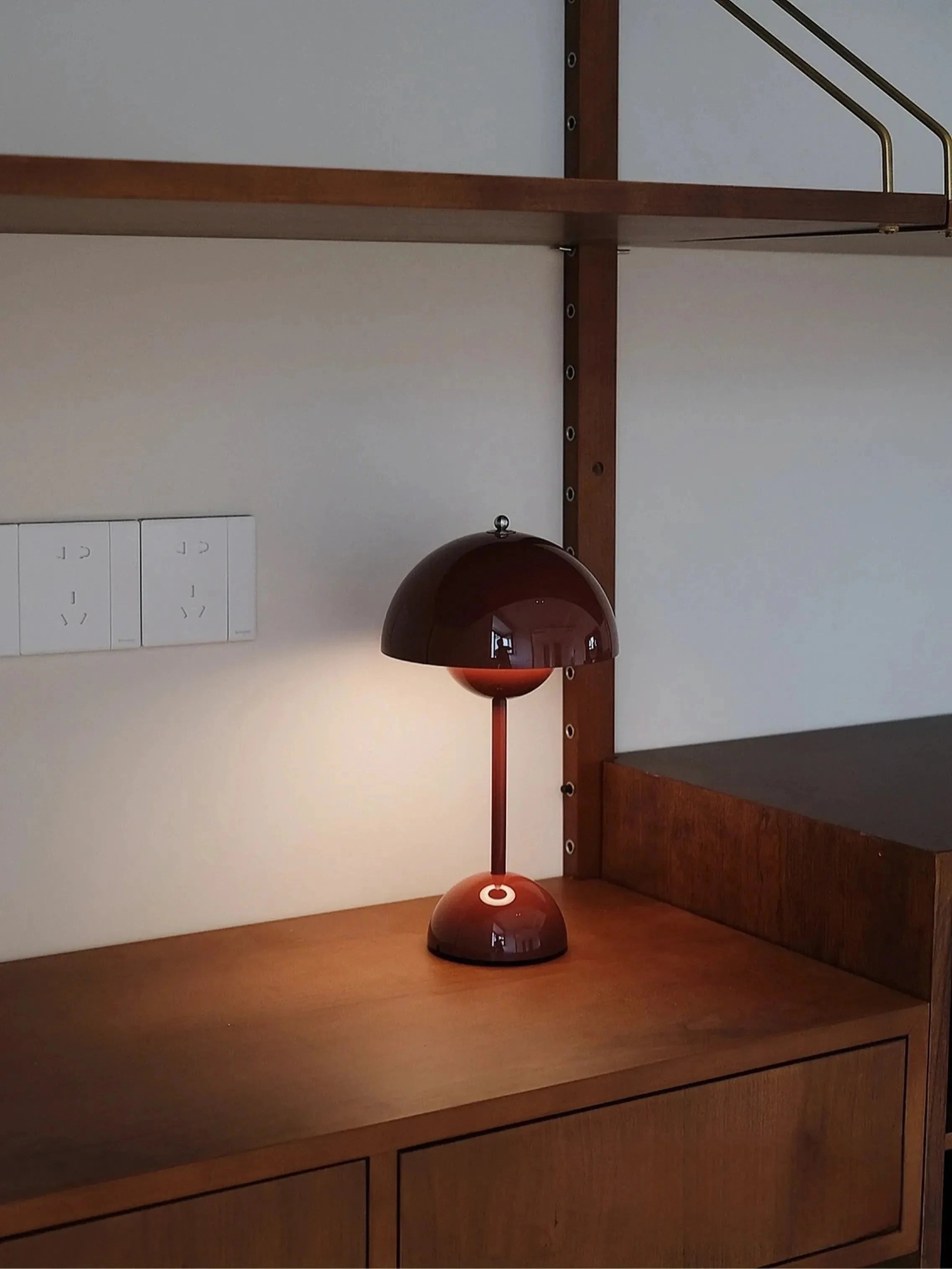 Vintage reddish-brown desk lamp with a wooden base, positioned on a table in a retro-themed home office setting, showcasing elements of interior design with surrounding flooring and wall decor.
