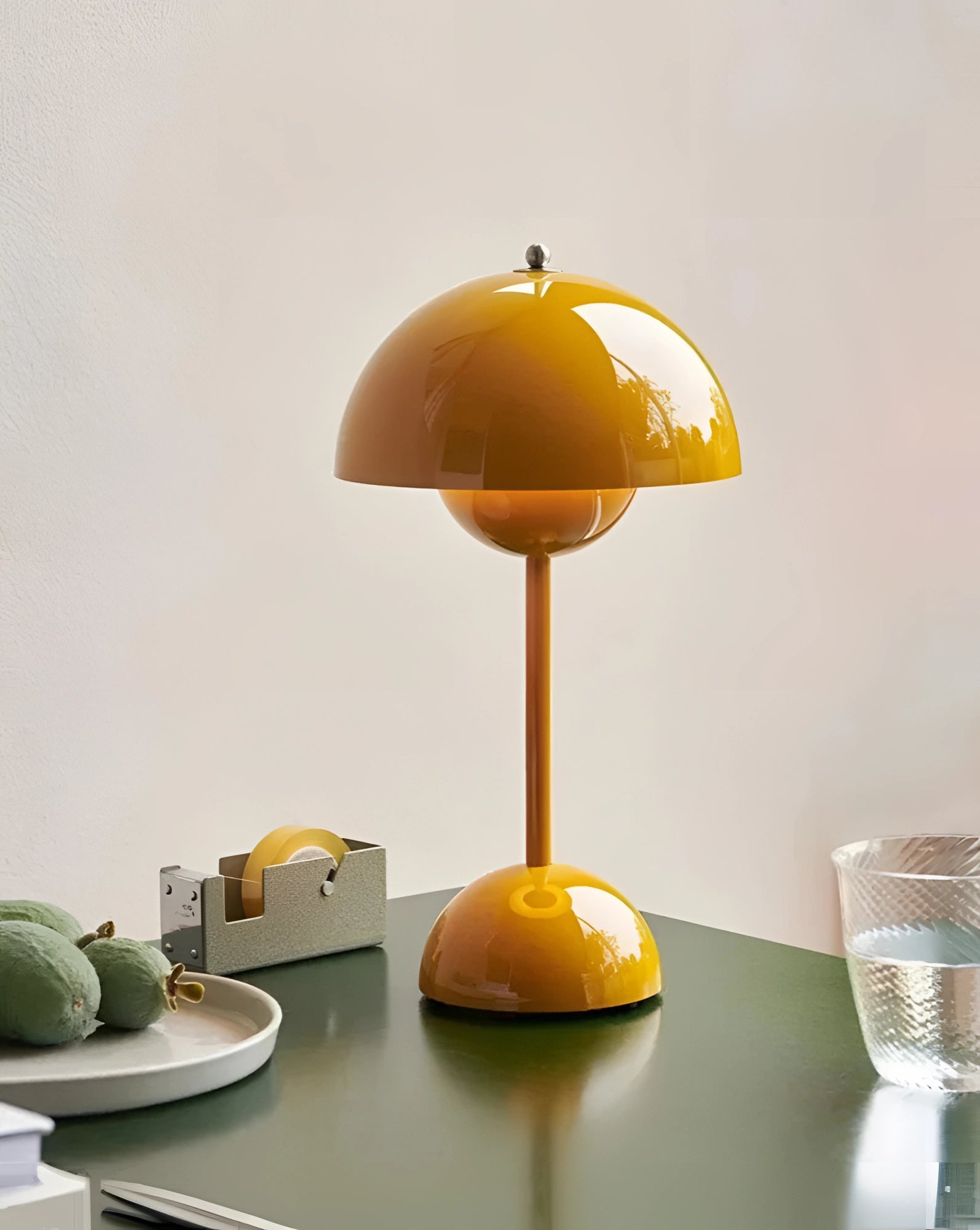 Vintage red desk lamp with a wooden base and a yellow lampshade, positioned on a table in a home office setting. The lamp is surrounded by a few decorative items including a small green plant, adding a retro and artistic touch to the room's decor.