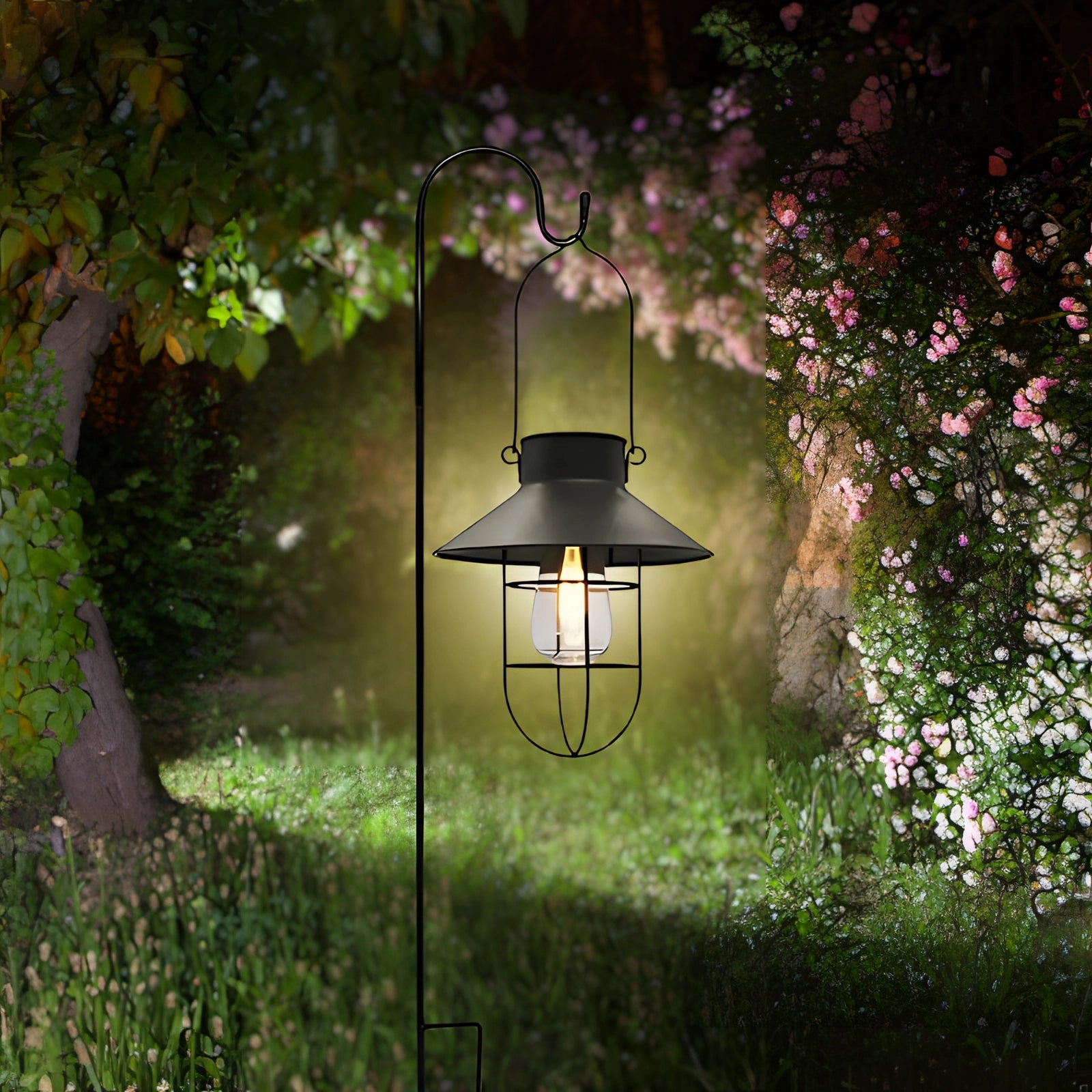 Vintage Solar LED Garden Lantern in black, hanging amidst a natural garden setting featuring lush greenery, shrubs, and trees. The lantern is designed to resemble a classic street light and is depicted amongst branches and grass, illustrating its suitability for eco-friendly outdoor lighting.