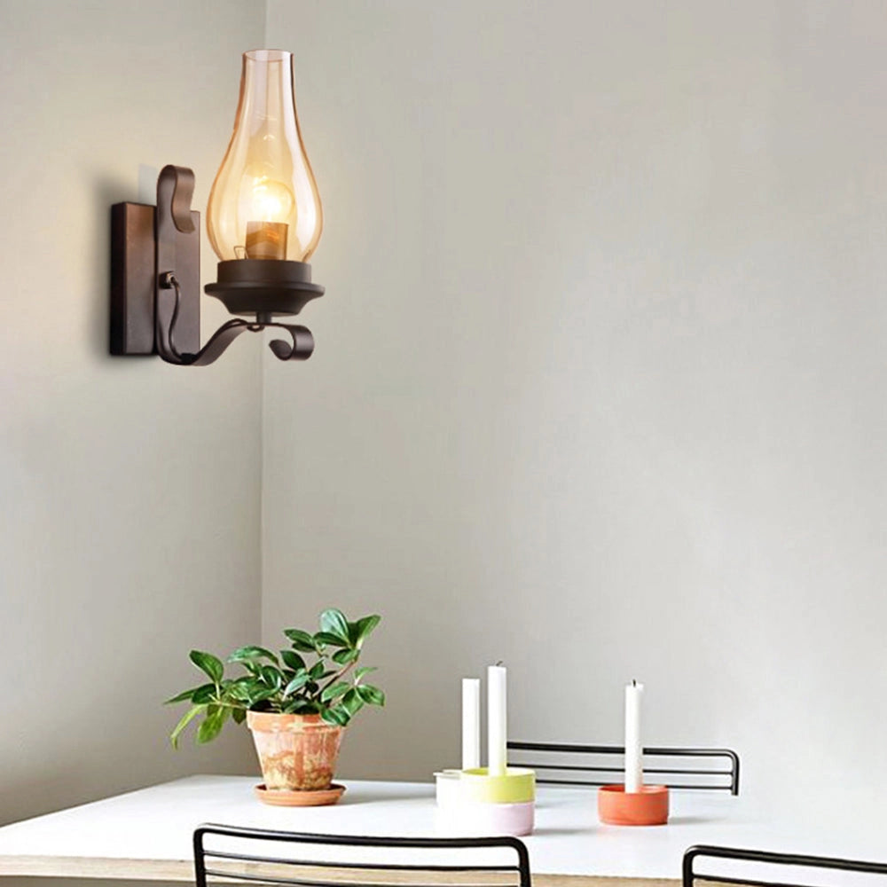 Vintage wall sconce featuring an antique lantern design made of rustic wrought iron, mounted on a wooden wall in a room with stylish interior design elements including a table and decorative plants.