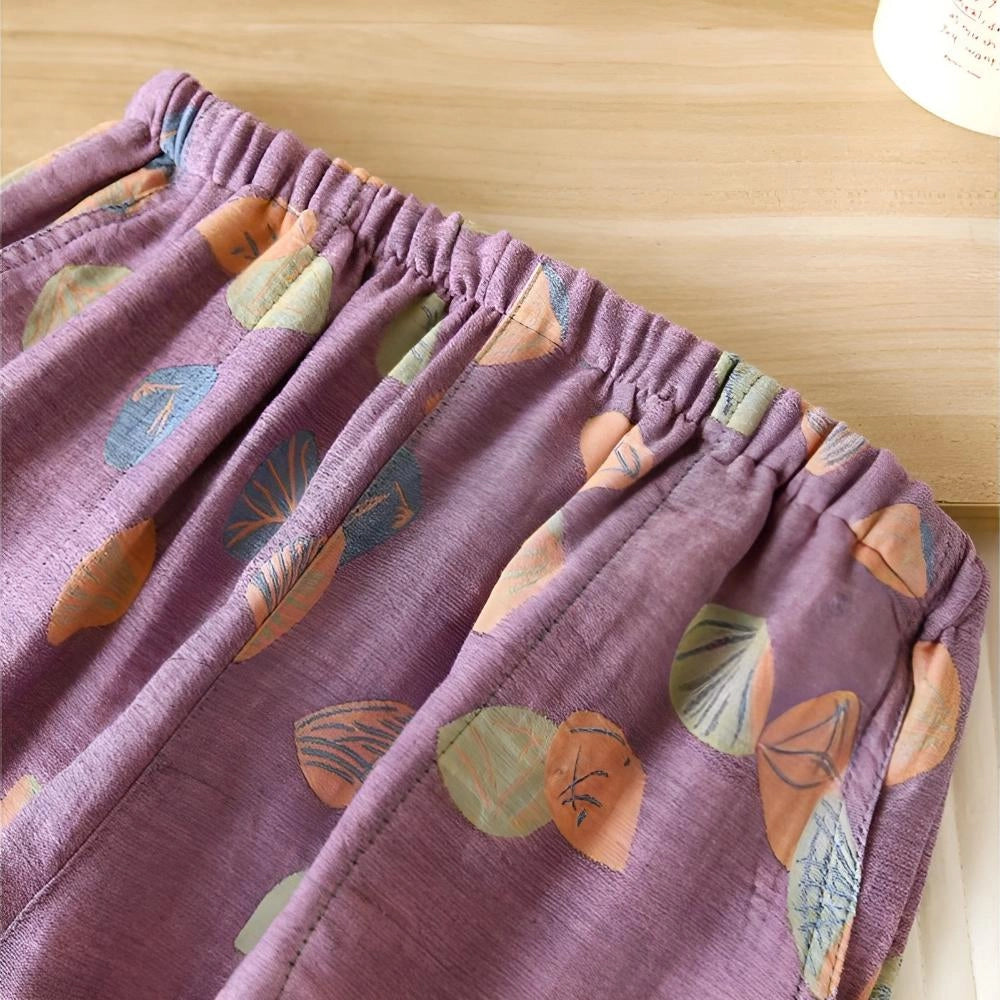 Colorful women's summer shorts featuring a vibrant leaf print design, with an elastic waistband for comfort. The fabric appears breathable and lightweight, predominantly in shades of purple and magenta, showcasing a stylish and creative textile pattern.
