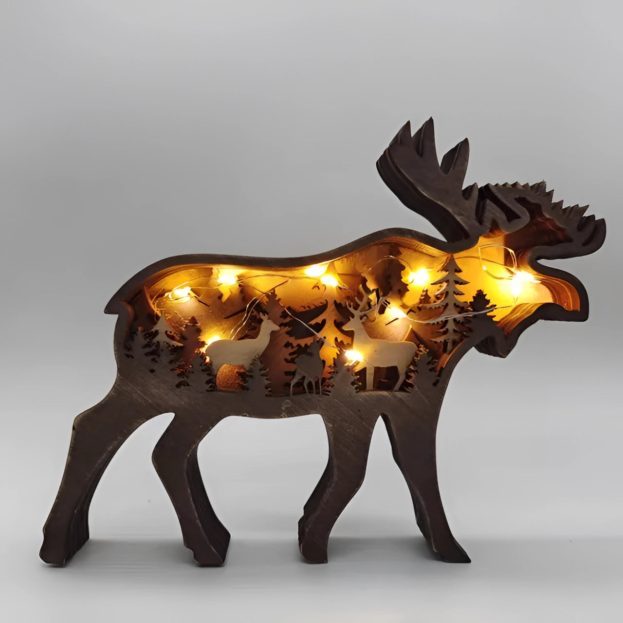 Wooden sculpture of a moose in a forest setting, featuring intricate carvings and rustic design, adorned with lights for decorative home decor.