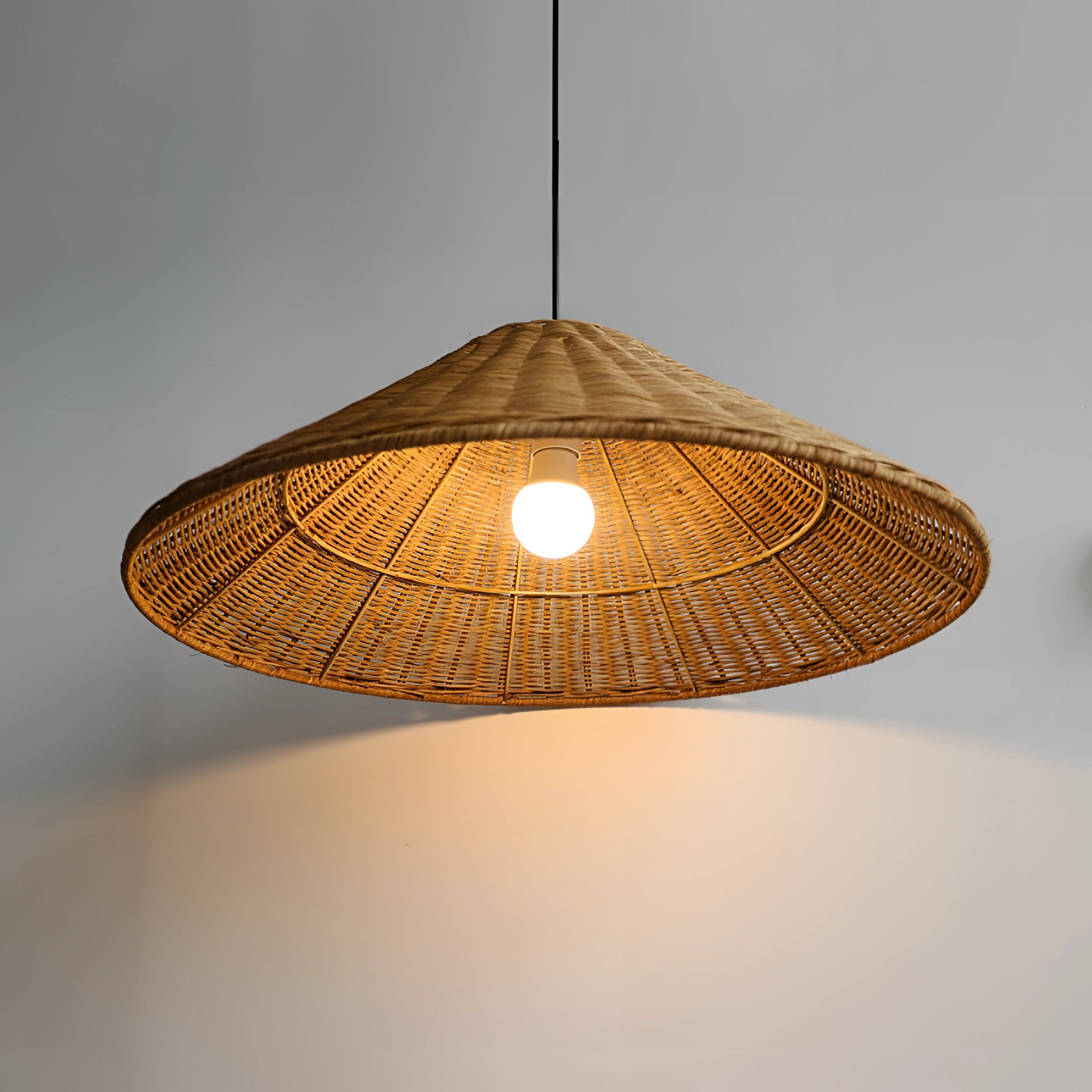 Eco-friendly woven rattan pendant light with a conical shape, ideal for Scandinavian decor, hanging from the ceiling with a warm amber glow.