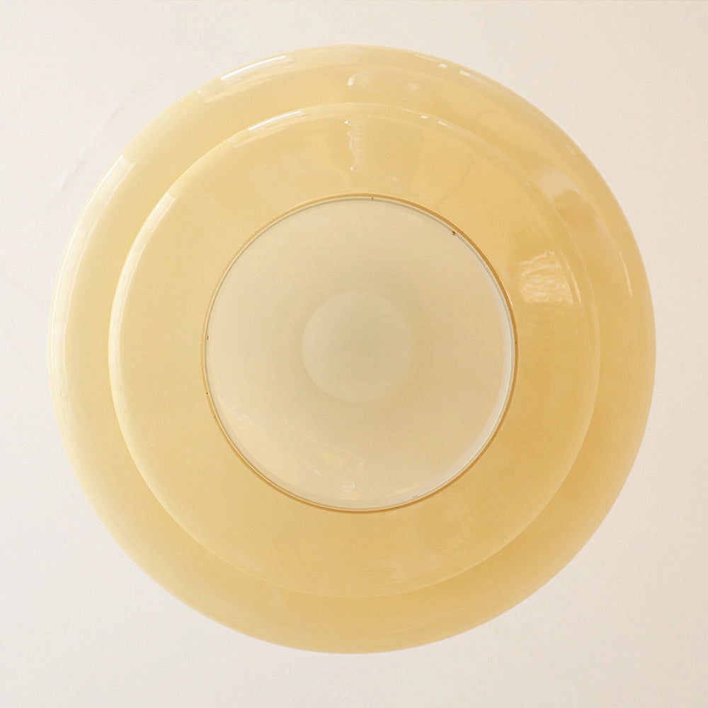 Yellow pendant light with modern Scandinavian minimalist design, hanging from the ceiling, illuminating a dining area with tableware including plates, cups, and porcelain dishware.